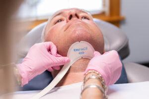 A BeachGlo Aesthetics provider wearing pink gloves applies Emface's submental applicator to a patient's chin for neck tightening in Nags Head.