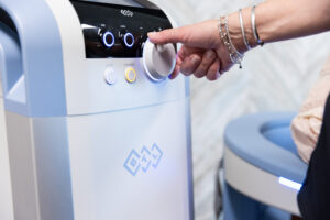 A female BeachGlo Aesthetics provider, wearing gold bracelets, adjusts the settings of the Emsella chair for a female patient. When combined with Emsculpt NEO, Emsella is effective for core strengthening in Nags Head, helping to relieve urinary incontinence.