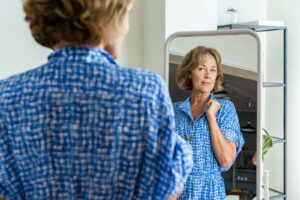 A patient examines herself in the mirror after receiving non-invasive neck tightening near Kill Devil Hills.