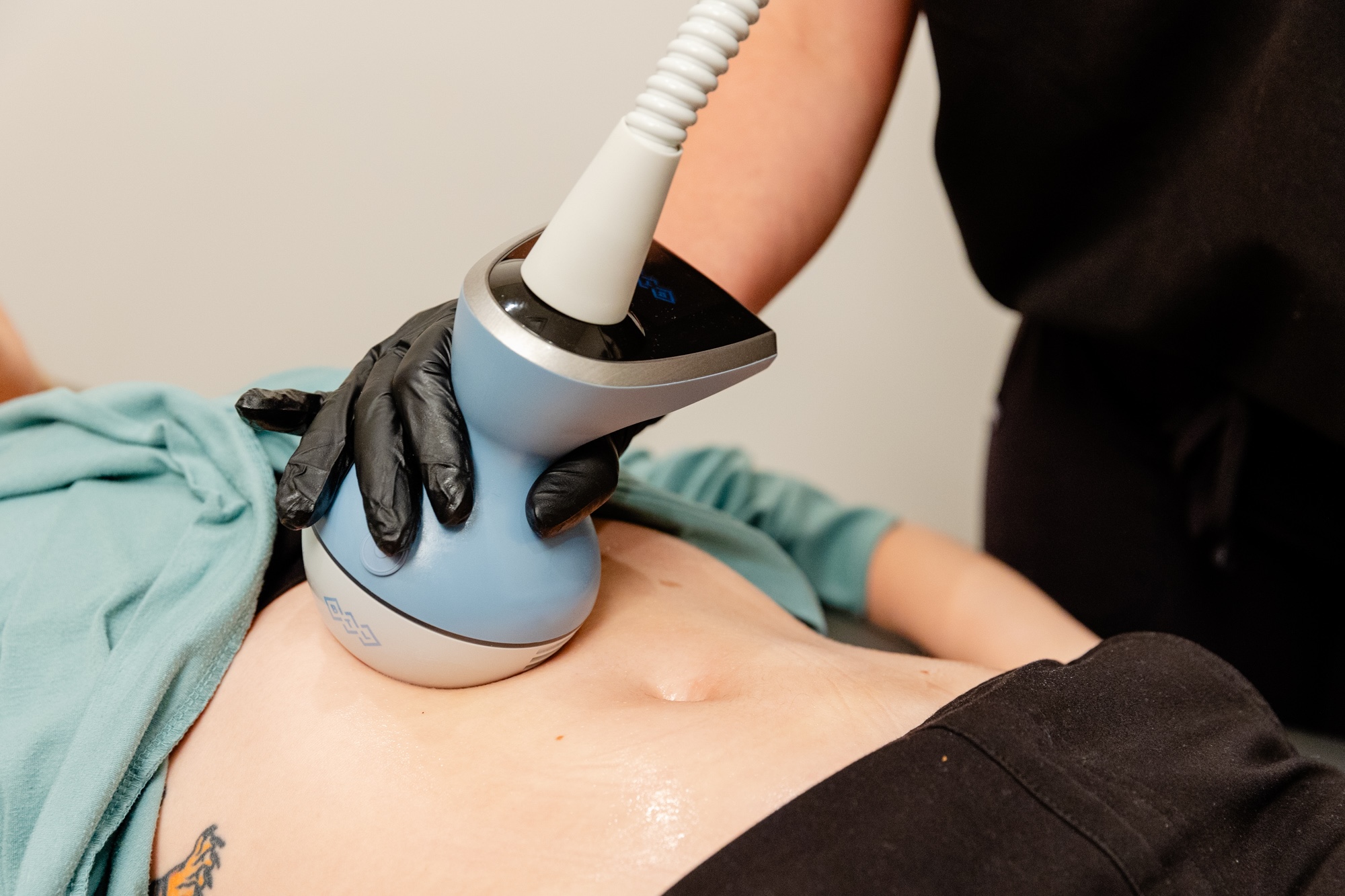 A woman laying down on the comfortable treatment table at BeachGlo Aesthetics while a provider administers Exion Body to her abdomen as the best way to lose belly fat in Nags Head.