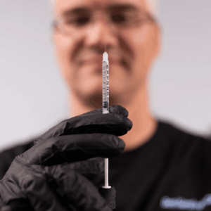 Co-founded Ben Kershner, wearing black scrubs and gloves, holds a syringe of Botox. Near Kitty Hawk, BeachGlo uses this cosmetic injectable for functional and aesthetic purposes.
